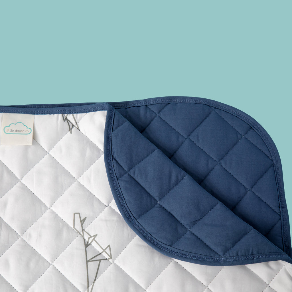 Close up of quilted corner of blanket showing blue fabric and dinosaur pattern on white background